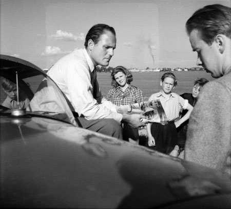 Claes Philip t.v. i samtal vid motorhuven på SE-AWU, medan en rökpelare stiger upp från pappersbrukets skorsten i bakgrunden. Foto: Åke Ahlstrand, Specialfoto