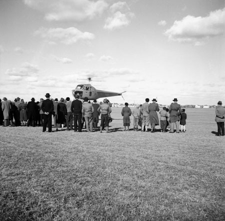 Helikoptern med Tybble och pappersbruksskorstenen i bakgrunden. Även gasklockans stålbur och gasverkets lägre skorstenar syns. Foto: Åke Ahlstrand, Specialfoto