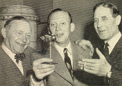 Sid 32: Albin Ahrenberg, Yngve Norrvi och generalmajor Paul af Uhr studerar en present till tidningen Looping på dess 1-årsdag. Det är Sven Wentzels vision av en flygande tunna.