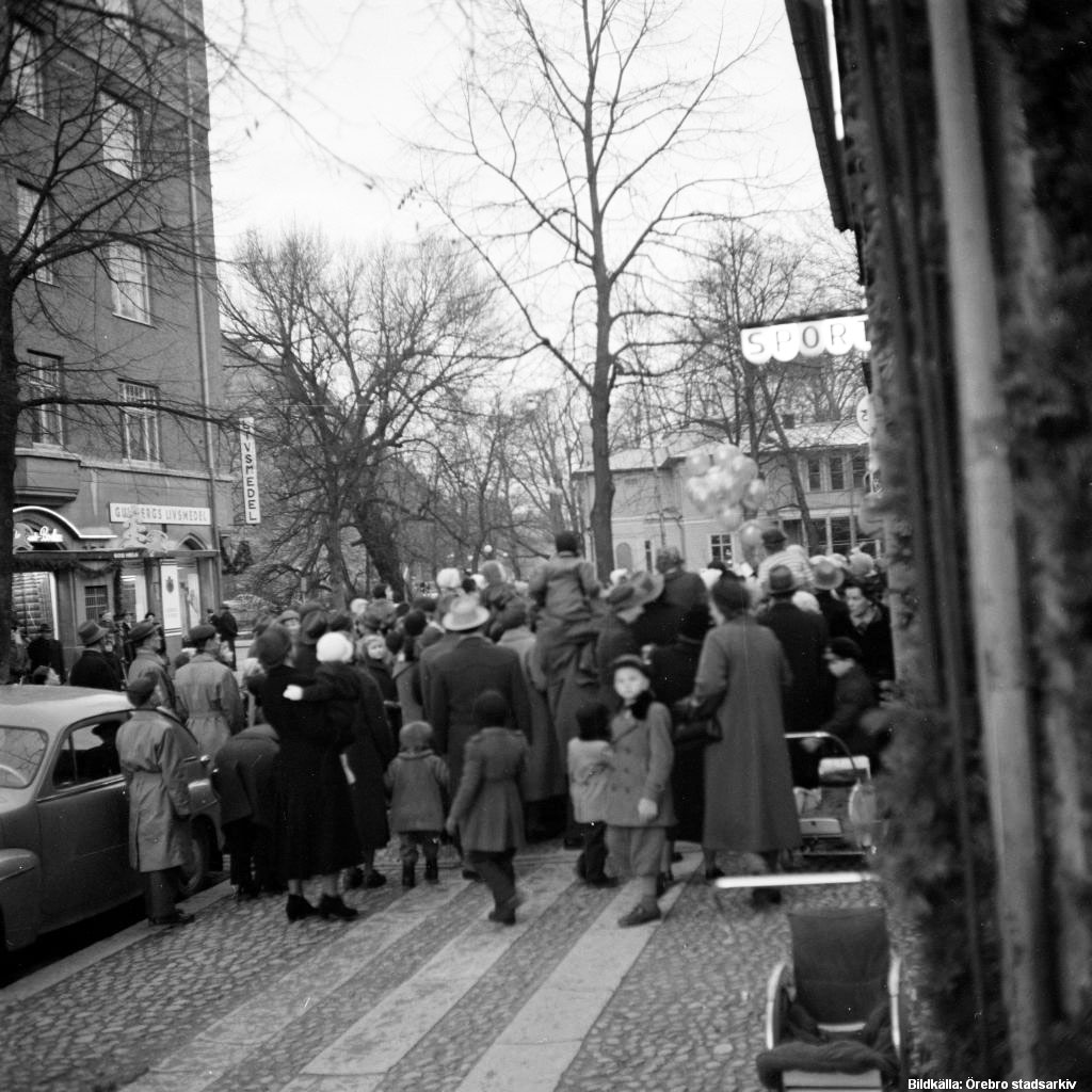 Kungsgatan den 4 dec 1955. Vy mot norr där den når Engelbrektsgatan. – Hörnbutiken på vänster sida är Gullbergs livsmedel med en vågrät och en lodrät vit skylt. – Det är samma stora hörnhus som syns i fonden på de två gatubilderna ovan. – Bildkälla: Örebro stadsarkiv/Erik Arlebo, bildnummer EKA-0283.